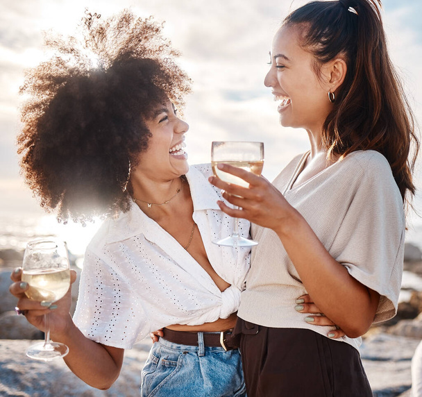 Two young mixed race female friends hanging out and having wine at the beach. Hispanic women having a glass on wine outdoors. - 写真・画像