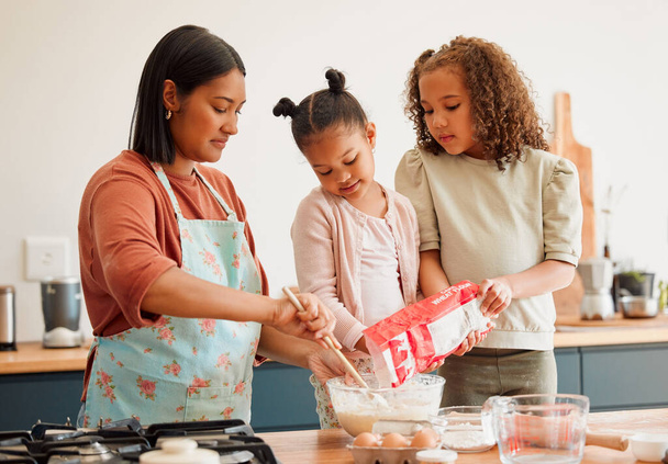 Females only, happy mixed race family of three cooking in a messy kitchen together. Loving black single parent bonding with her daughters while teaching them domestic skills at home. - 写真・画像