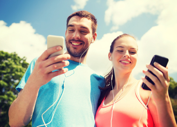 dos personas sonrientes con teléfonos inteligentes al aire libre
 - Foto, Imagen