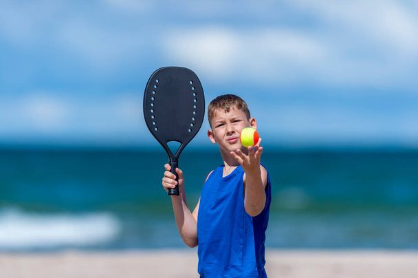Mladý chlapec hraje tenis na pláži. Dětský sportovní koncept. Horizontální sportovní motiv plakát, pohlednice, záhlaví, webové stránky a aplikace - Fotografie, Obrázek
