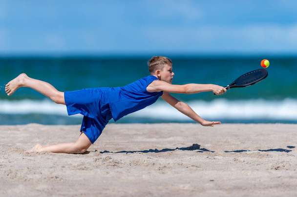 Мальчик играет в теннис на пляже. Детская спортивная концепция. Горизонтальный плакат спортивной тематики, поздравительные открытки, заголовки, веб-сайт и приложение - Фото, изображение
