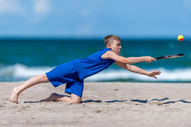 Young boy playing tennis on beach. Kids sport concept. Horizontal sport theme poster, greeting cards, headers, website and app - Photo, Image