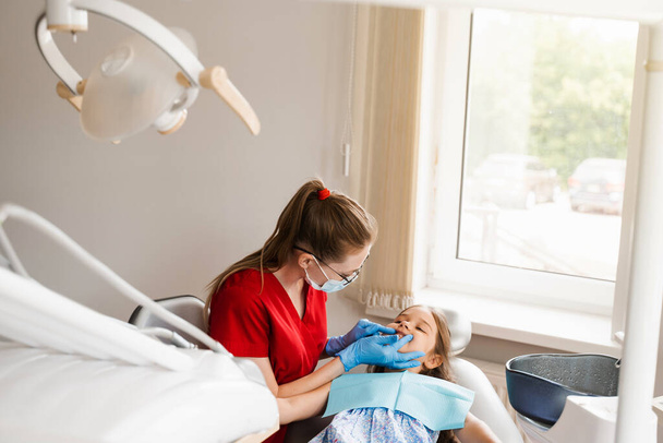 Consultation with child dentist at dentistry. Teeth treatment. Children dentist examines girl mouth and teeth and treats toothaches. Happy child patient of dentistry - Foto, afbeelding