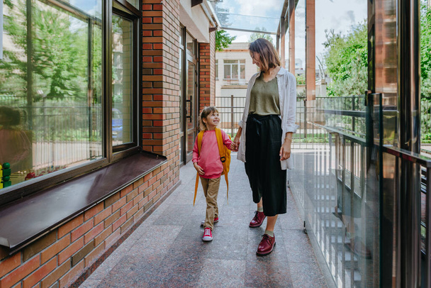 Mother leading her daughter at school. Young woman and little 6 years old girl near elementary school building. Back to school concept. - Foto, immagini