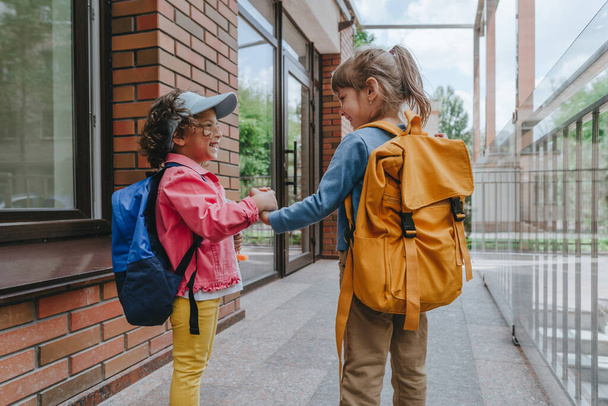 Back view of two little girls with backpacks going to an elementary school. Back to school concept. Selective focus on girls. - Fotografie, Obrázek