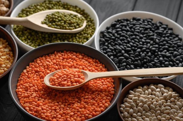 Overhead view of bowls of assorted raw legumes on a dark wooden table - Foto, afbeelding