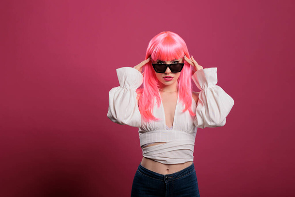 Confident attractive girl with trendy sunglasses and glamour style standing over pink background in studio. Carefree sexy woman with stylish eyewear posing and having fun on camera. - Фото, изображение