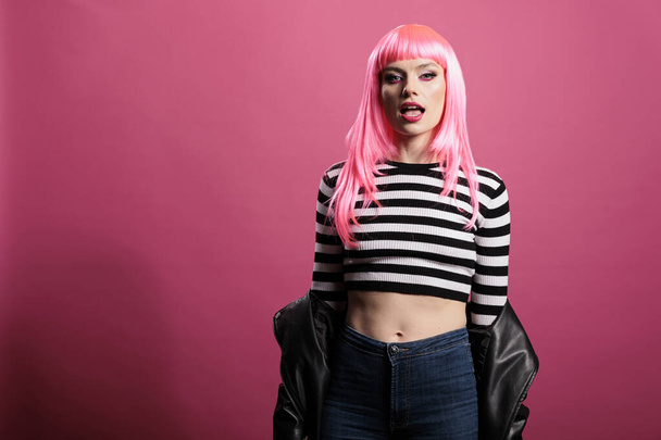 Atraktivní okouzlující model s růžovými vlasy a koženou bundou sedí na pozadí studia, pocit sebevědomí a funky s trendy rocker stylu. Nošení smyslné sexy a punk módní položky. - Fotografie, Obrázek
