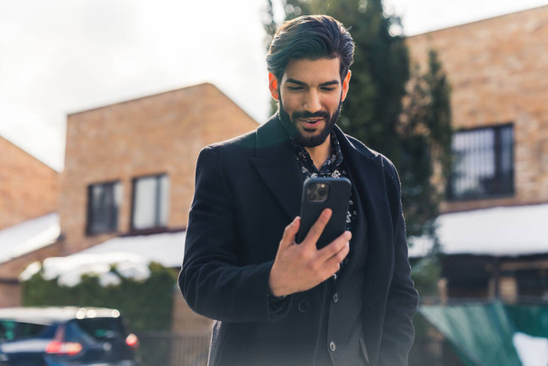 Handsome Latin man talking through his telephone while walking outdoors. High quality photo - Photo, Image