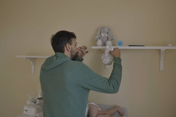 40-year-old father changing diaper of his newborn son. Family life of single father. Father can't stand the smell of his baby's poopy diaper. - 写真・画像