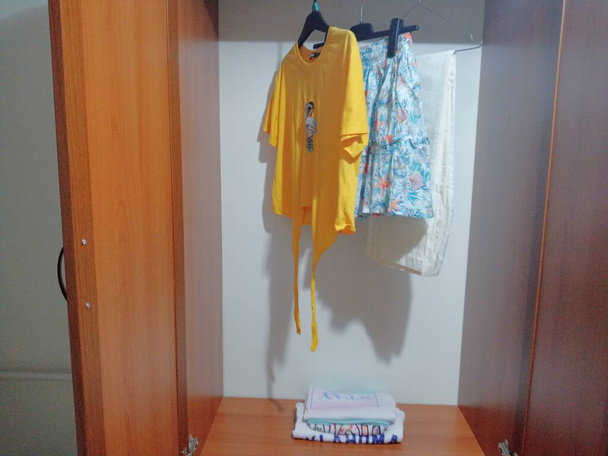 Három ruha lóg a vállfán a szekrényben. Pólók, szoknyák, nyári nadrág. - Fotó, kép