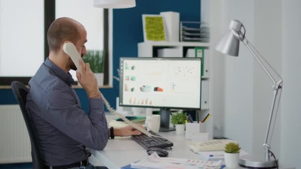 Company secretary talking on landline phone call at desk, working on business project with charts and graphs. Office worker having conversation on telephone and planning strategy. - Filmmaterial, Video