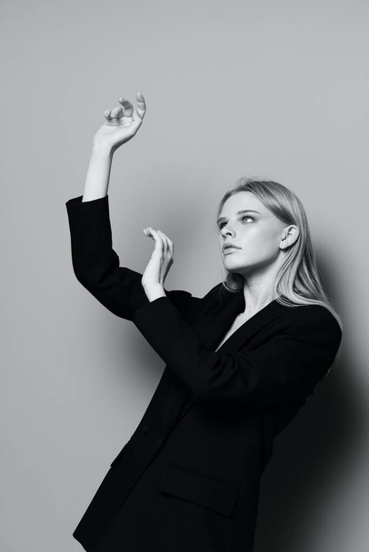 Μόδα μοντέλο κορίτσι ποζάρουν με τα χέρια ψηλά στο στούντιο σε μαύρο και άσπρο στυλ σε ένα κλασικό σακάκι. Υψηλής ποιότητας φωτογραφία - Φωτογραφία, εικόνα