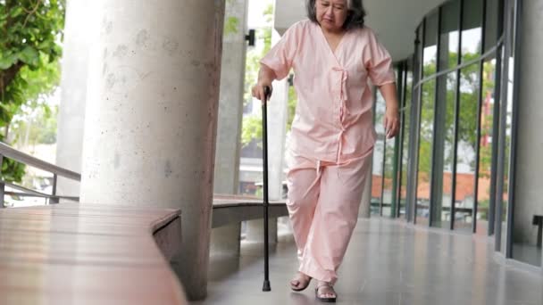 Aasialainen iäkäs naispotilas pitelee keppiä auttaakseen kävelemään fysioterapiassa Hänellä oli kipua jaloissa ja polvissa. Sairauden käsite vanhuksilla. Polvikipu. terveydenhuolto - Materiaali, video