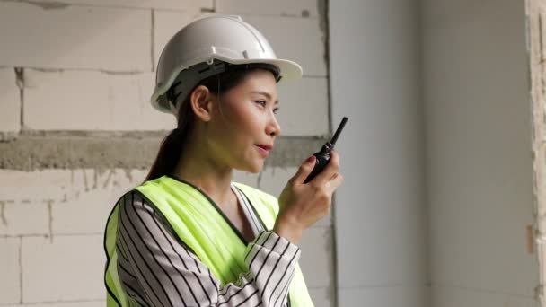 建設現場で白いヘルメットをかぶっているアジアの女性エンジニア建築請負業者と通信するための無線を保持しています。建設業の概念. - 映像、動画