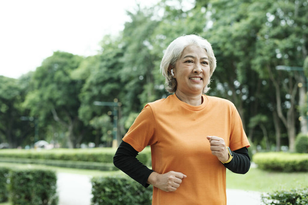 Athletic asian senior woman running in the morning outdoor jogging in park. - Photo, image