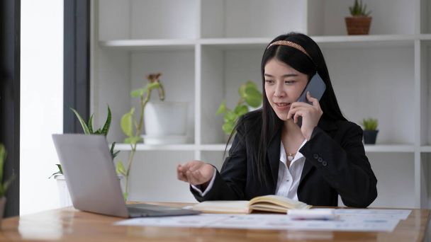 Азійська бізнесменка розмовляє по телефону з клієнтом в офісі. - Фото, зображення