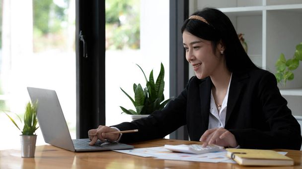 Beautiful Asian businesswoman analyzes charts using laptop calculator at the office - Photo, image