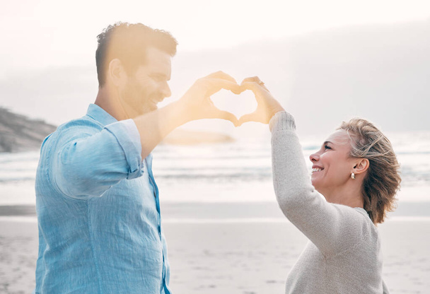 Can you feel the love. a mature couple making a heart shape with their hands at the beach - Foto, immagini
