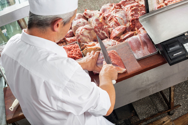 Male Butcher Cutting Meat At Display Cabinet - Фото, изображение
