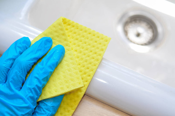 primo piano in guanti blu con straccio giallo per pulire fango, concetto di pulizia, faccende domestiche - Foto, immagini