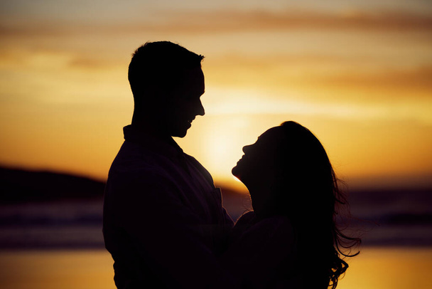 Silhouette couple enjoying romantic moment standing face to face looking into eyes at sunset. Unknown boyfriend and girlfriend feeling in love while bonding at the beach. - 写真・画像