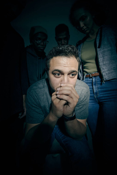 One mixed race male suffering mental illness in asylum. Caucasian schizophrenic man experiencing a depression while being surrounded by people on a stage theatre performance. - Photo, image