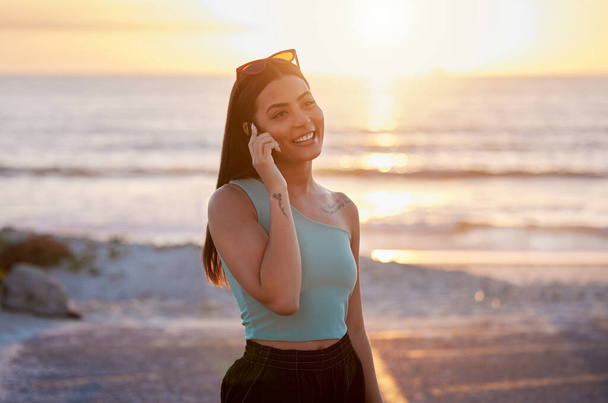 a beautiful young female talking on her cellphone while enjoying time at the beach. - 写真・画像