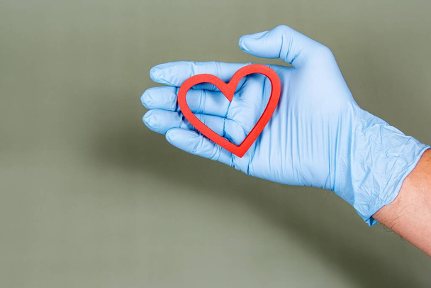 Cirurgical gloved hand holding a heart shape - Φωτογραφία, εικόνα