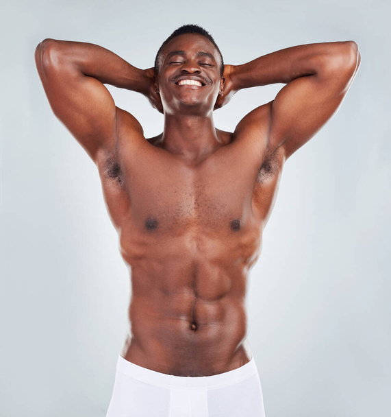 Portrait of a smiling African American fitness model posing topless in a underwear and looking muscular. Happy black male athlete isolated on grey copyspace in a studio wearing boxers. - Fotó, kép