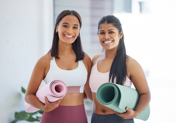 Portrait of two sporty young women holding exercise mats in a yoga studio. - Foto, imagen