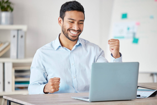 Mladý šťastný a vzrušený smíšený podnikatel jásající pěstí, zatímco pracuje sám na laptopu v kanceláři v práci. Jeden hispánský šéf se usmívá při oslavě úspěchu. - Fotografie, Obrázek