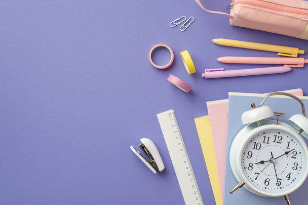 Back to school concept. Top view photo of colorful stationery notebooks alarm clock pens pink pencil-case adhesive tape clips ruler and stapler on isolated violet background - Foto, Imagen