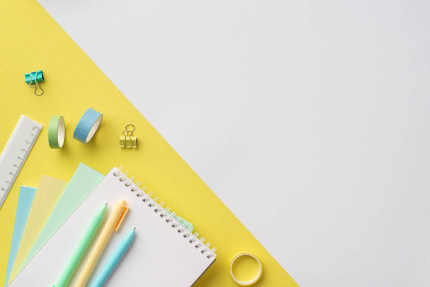 Вернемся к школьной концепции. Фото школы поставляет копировальные книги ручки линейки клейкой ленты и зажимы связующего на двухцветном желтом и белом фоне с копипространством - Фото, изображение