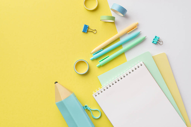 School accessories concept. Top view photo of blue pencil-case stack of copybooks colorful pens binder clips and adhesive tape on bicolor yellow and white background - Photo, image