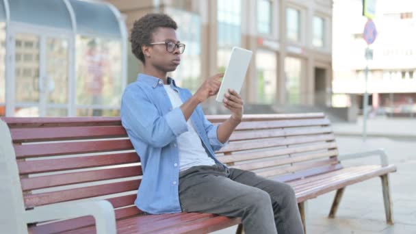 Африканський чоловік користується планшетом, сидячи на вулиці на лаві - Кадри, відео