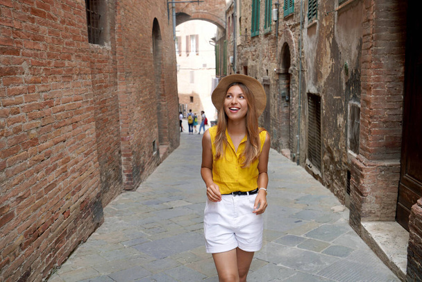 Holidays in Tuscany. Beautiful stylish tourist girl walking between narrow alleys of Siena historic town of Tuscany, Italy. - Photo, Image