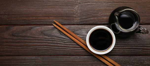 Soy sauce and chopsticks on dark wooden background with space for text, top view - Valokuva, kuva