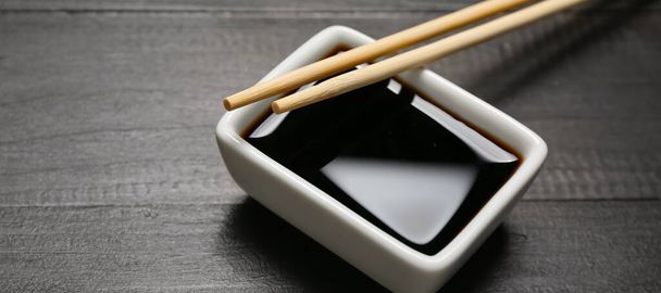 Bowl of soy sauce and chopsticks on dark wooden background, closeup - Фото, изображение