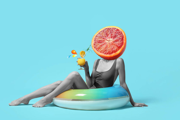 Woman with ripe orange instead of her head, cocktail and swimming ring on blue background - Photo, image