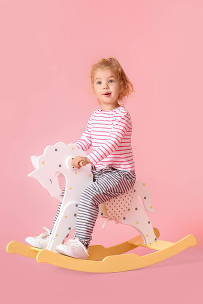 Adorable little girl in bunny ears with rocking horse on pink background - Фото, зображення