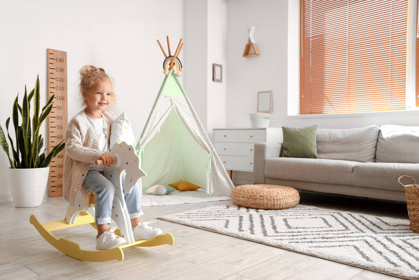 Cute little girl with pillow and rocking horse at home - Fotoğraf, Görsel