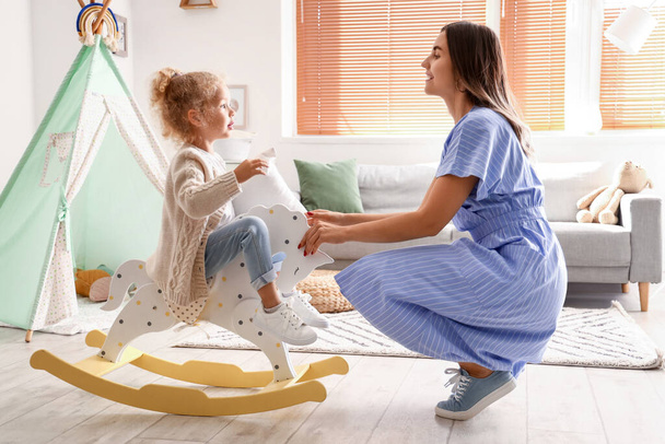 Cute little girl with pillow, rocking horse and her mother at home - Photo, Image