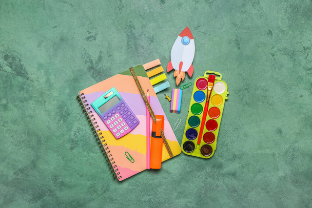 Paper rocket with school stationery on green background - 写真・画像