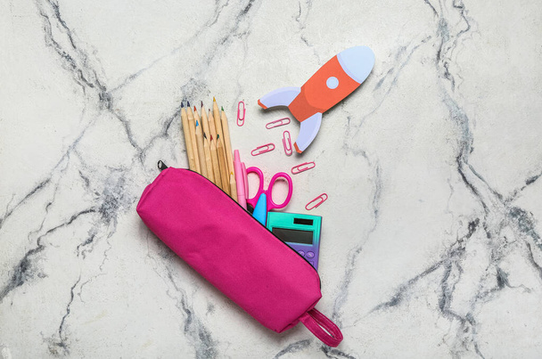 Pencil case with school stationery and paper rocket on light background - Foto, afbeelding