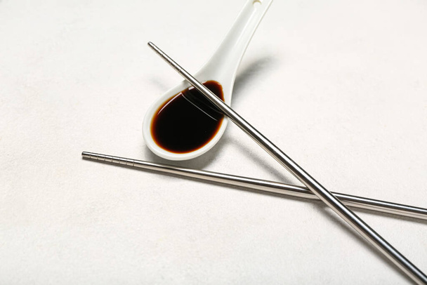 Spoon of soy sauce and chopsticks on white background - 写真・画像