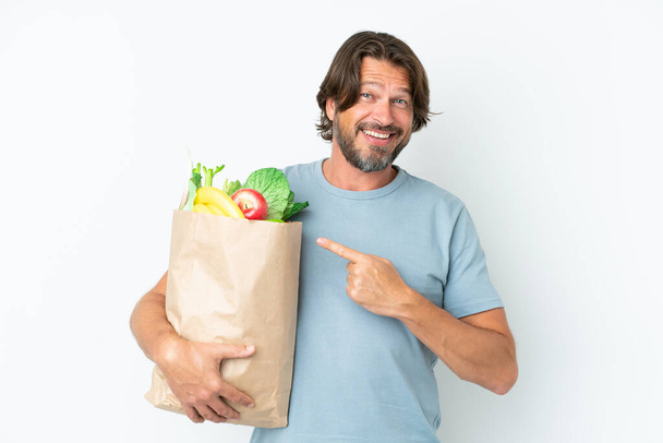 Senior dutch man holding grocery shopping bag over isolated background pointing to the side to present a product - Foto, Bild