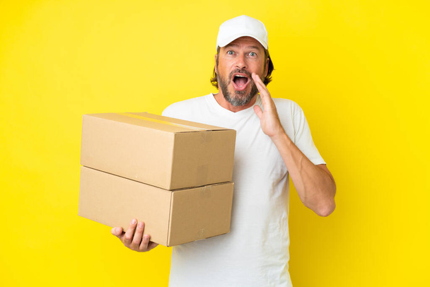 Delivery senior dutch man isolated on yellow background with surprise and shocked facial expression - 写真・画像