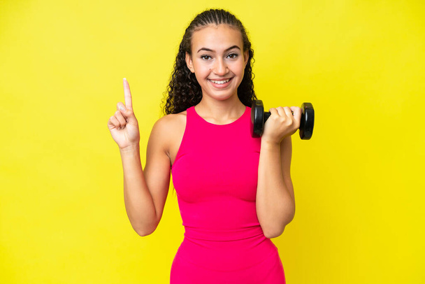 Young sport woman making weightlifting isolated on yellow background pointing up a great idea - Foto, Imagem