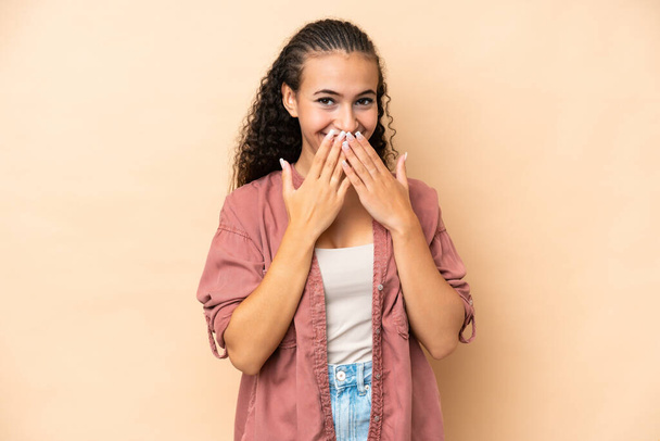 Young woman isolated on beige background happy and smiling covering mouth with hands - Photo, image